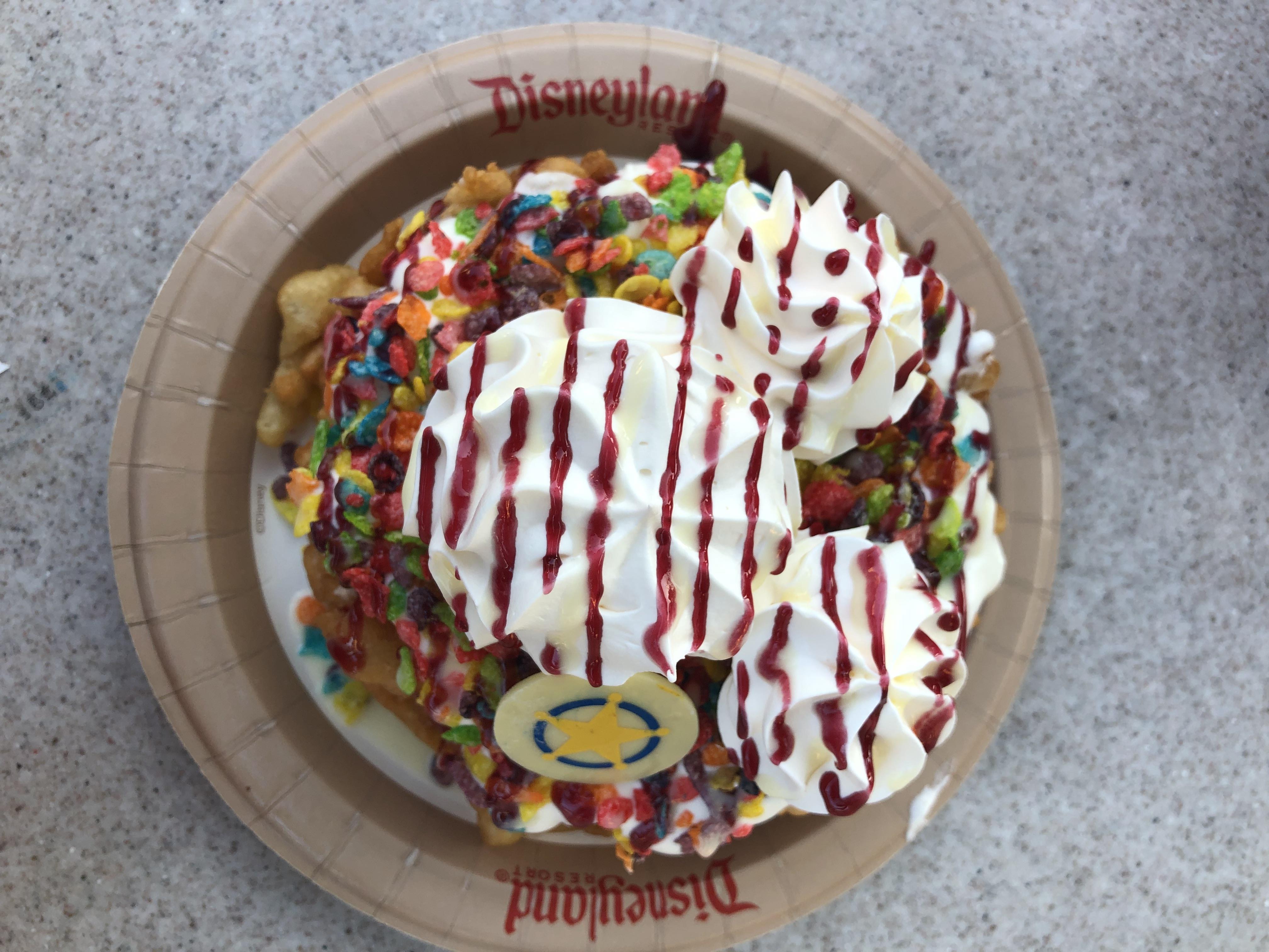 A plate of funnel cake, covered in fruity pebbles and whipped cream shaped like Mickey Mouse ears.